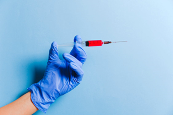 Hand with a glove on holding a needle filled with a red liquid